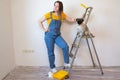 Happy woman makes repairs in her apartment. Funny female with a roller on ladder with copy space. Independent single Royalty Free Stock Photo