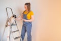 Happy woman makes repairs in her apartment. Funny female with a roller on ladder with copy space. Independent single Royalty Free Stock Photo