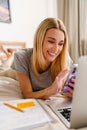 Happy woman making notes and using cellphone while lying in bed at home Royalty Free Stock Photo