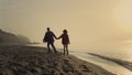 Happy woman and man walking on sea beach. Lovely couple holding hands at sunrise Royalty Free Stock Photo