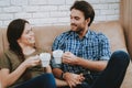 Happy Woman and Man with White Cups on Brown Sofa.