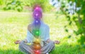 Woman is meditating in the lotus pose with glowing seven chakras on grass. Woman is practicing yoga on the park Royalty Free Stock Photo