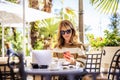 Happy woman with mobile phone and laptop sitting at outdoor cafe in summer Royalty Free Stock Photo