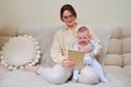 Happy woman mother with infant baby watching in digital tablet while sitting on home sofa in living room Royalty Free Stock Photo