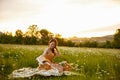 a happy woman in an orange dress sits in a meadow of daisies during sunset and looks at her hat Royalty Free Stock Photo