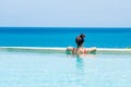 Happy woman in orange swimsuit swimming in infinity pool at luxury hotel against ocean front. young female enjoy in tropical Royalty Free Stock Photo