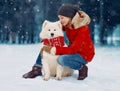 Happy woman owner petting embracing white Samoyed dog outdoors wearing red scarf while sitting on snow in winter snowy day Royalty Free Stock Photo