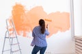 Dancing funny woman painting interior wall with paint roller in new house. A woman with roller applying paint on a wall. Royalty Free Stock Photo
