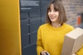 Happy woman with parcel and phone standing near automatic post terminal