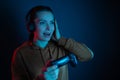 Happy woman playing online video game, keeps headphone and joystick on dark blue background. Gaming concept. Funny entertainment