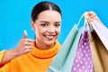 Happy woman, portrait smile and shopping bags with thumbs up for purchase, sale or discount against blue studio Royalty Free Stock Photo