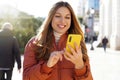 Happy woman in puffer jacket using yellow smart phone in the city street