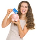 Happy woman putting credit card into piggy bank