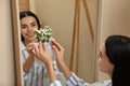 Happy woman putting flowers into silicone vase attached to mirror in room Royalty Free Stock Photo