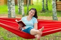Happy woman reading a book, sitting in a red hammock Royalty Free Stock Photo