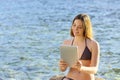 Happy woman reading a tablet reader on the beach seaside