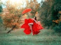 Happy woman in red dress with an umbrella flies in air. Long bare legs in dance.