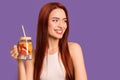 Happy woman with red dyed hair and refreshing grapefruit drink on purple background