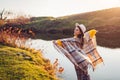 Happy woman relaxing by autumn lake at sunset. Stylish girl in hat plays with wind and scarf enjoying fall landscape Royalty Free Stock Photo