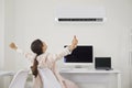 Happy woman relaxing at her office desk under cool, fresh air flowing from the air conditioner