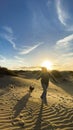 Happy woman run on the sand dunes with her two puppy dogs having fun and enjoying the colorful sunset in background. Tourists at Royalty Free Stock Photo