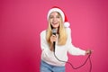 Happy woman in Santa hat singing with microphone on pink background. Christmas music Royalty Free Stock Photo