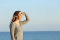 Happy woman searching on the beach with hand on forehead