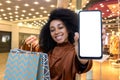 Happy woman shopper in supermaket smiling and looking at camera, holding colorful shopping bags in hands, showing phone Royalty Free Stock Photo