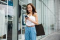 Happy woman with shopping bags, browsing her smartphone outside a fashion store Royalty Free Stock Photo