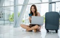 woman sitting on the airport floor, typing on her phone and laptop Royalty Free Stock Photo
