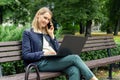 happy woman sitting on the bench in the city park and talking on the mobile phone while using laptop Royalty Free Stock Photo