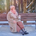 A happy woman is sitting on a bench with a lantern in her hands, a winter park with snow-covered trees Royalty Free Stock Photo