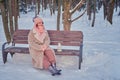 A happy woman is sitting on a bench with a lantern in her hands, a winter park with snow-covered trees Royalty Free Stock Photo