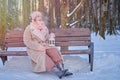 A happy woman is sitting on a bench with a lantern in her hands, a winter park with snow-covered trees Royalty Free Stock Photo