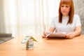 Happy woman sitting and calculating bills in the home office.Money house from dollar banknote on wooden table. Royalty Free Stock Photo