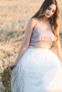 Happy woman sitting on hay stack walking in summer evening, beautiful romantic girl with long hair outdoors in field at sunset Royalty Free Stock Photo