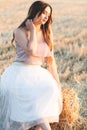 Happy woman sitting on hay stack walking in summer evening, beautiful romantic girl with long hair outdoors in field at sunset Royalty Free Stock Photo