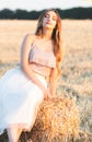 Happy woman sitting on hay stack walking in summer evening, beautiful romantic girl with long hair outdoors in field at sunset Royalty Free Stock Photo