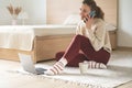 Happy woman sitting with laptop on floor in cozy bedroom and joyful talking using cellphone Royalty Free Stock Photo