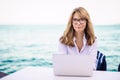 Happy woman sitting by the sea and using laptop while looking at camera and smiling Royalty Free Stock Photo