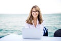 Happy woman sitting by the sea and using laptop while looking at camera and smiling Royalty Free Stock Photo