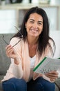 happy woman sitting at table and solve crosswords