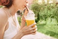 Woman with slim figure drinks freshly squeezed orange juice from a plastic cup. Useful and harmful beverages