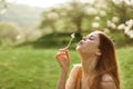 The happy woman smiles and blows the dandelion in the wind. Summer green landscape and sunshine in the background