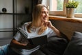 Happy woman smiling and reading book while sitting on sofa at home Royalty Free Stock Photo