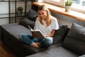 Happy woman smiling and reading book while sitting on sofa at home Royalty Free Stock Photo