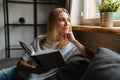 Happy woman smiling and reading book while sitting on sofa at home Royalty Free Stock Photo