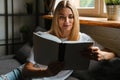 Happy woman smiling and reading book while sitting on sofa at home Royalty Free Stock Photo