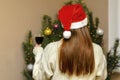 Happy woman standing against Christmas tree at home with wine glass.red hair lady in santa claus hat celebrating new year.Merry Royalty Free Stock Photo