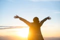 Woman standing alone with arms raised up during beautiful sunrise at the morning.